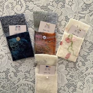 May include: Four rectangular felt pouches in blue, orange, and white, each featuring a button closure and a small white card tucked inside. The cards display the text 謝謝 and gracias. The pouches have varied textures and decorative details.
