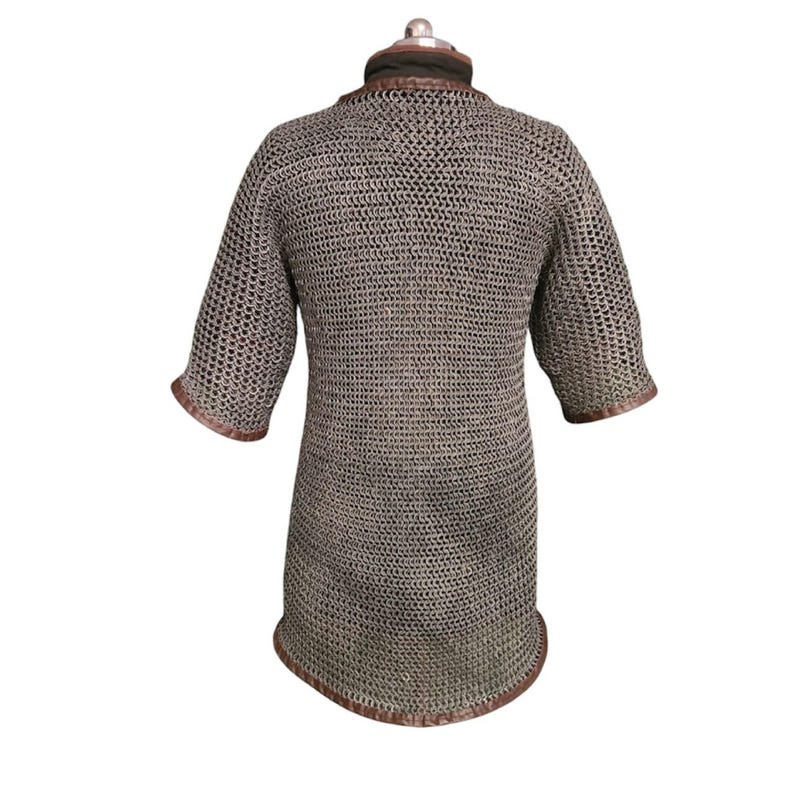 May include: A silver chainmail shirt with brown leather trim around the neck, sleeves, and bottom. The shirt is on a mannequin.