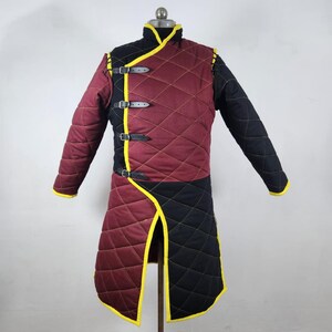 May include: A quilted gambeson with a burgundy and black color scheme. The gambeson has a yellow trim and is secured with leather straps.