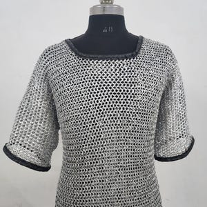 May include: A silver chainmail shirt with short sleeves and a square neckline. The edges of the sleeves and neckline are trimmed with black material. The shirt is displayed on a black mannequin.