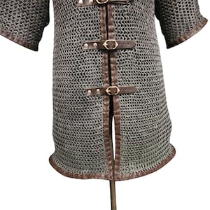 May include: A gray chainmail shirt with brown leather straps and trim. The shirt has a split front and short sleeves.