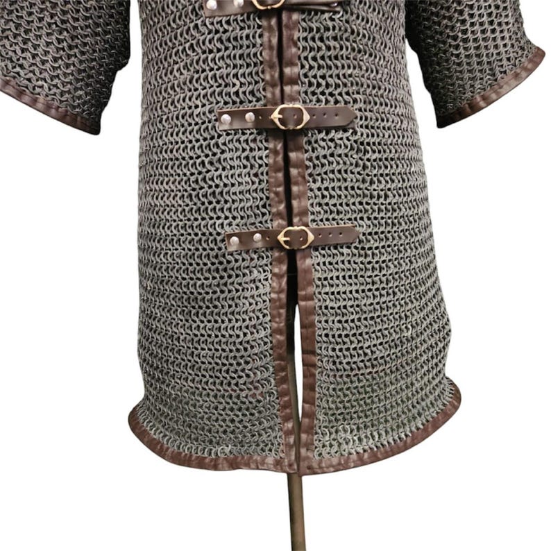 May include: A gray chainmail shirt with brown leather straps and trim. The shirt has a split front and short sleeves.
