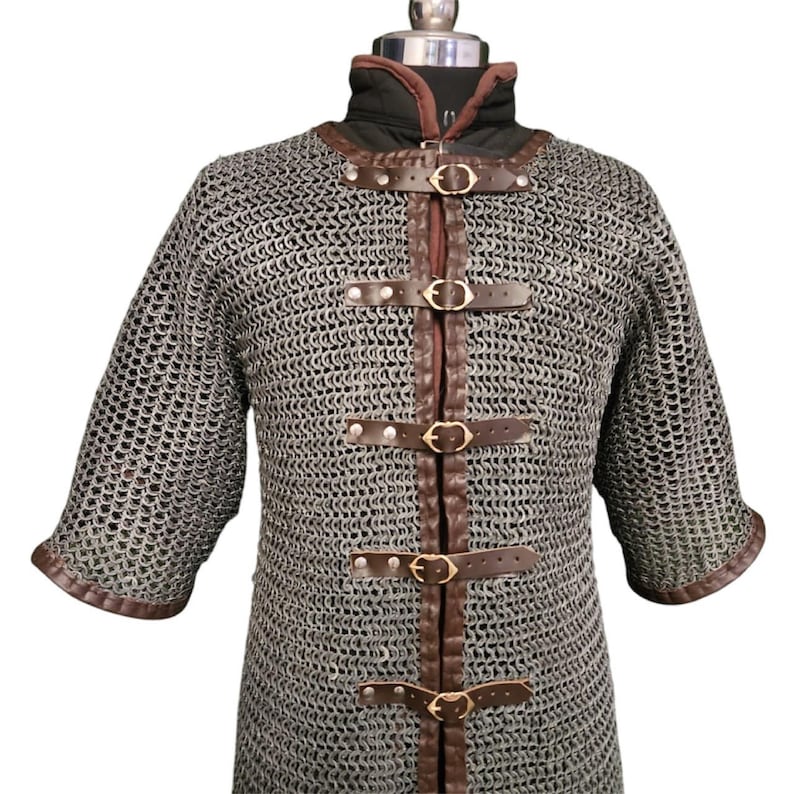 May include: A silver chainmail shirt with brown leather straps and buckles. The shirt has long sleeves and a high neckline.
