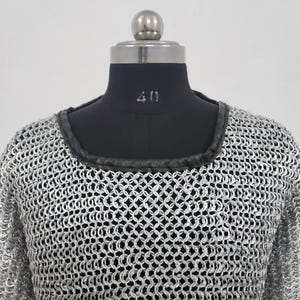 May include: A silver chainmail shirt with a black leather trim around the neckline. The shirt is displayed on a black mannequin with the number 40 visible. The chainmail is made of small, interlocking metal rings.