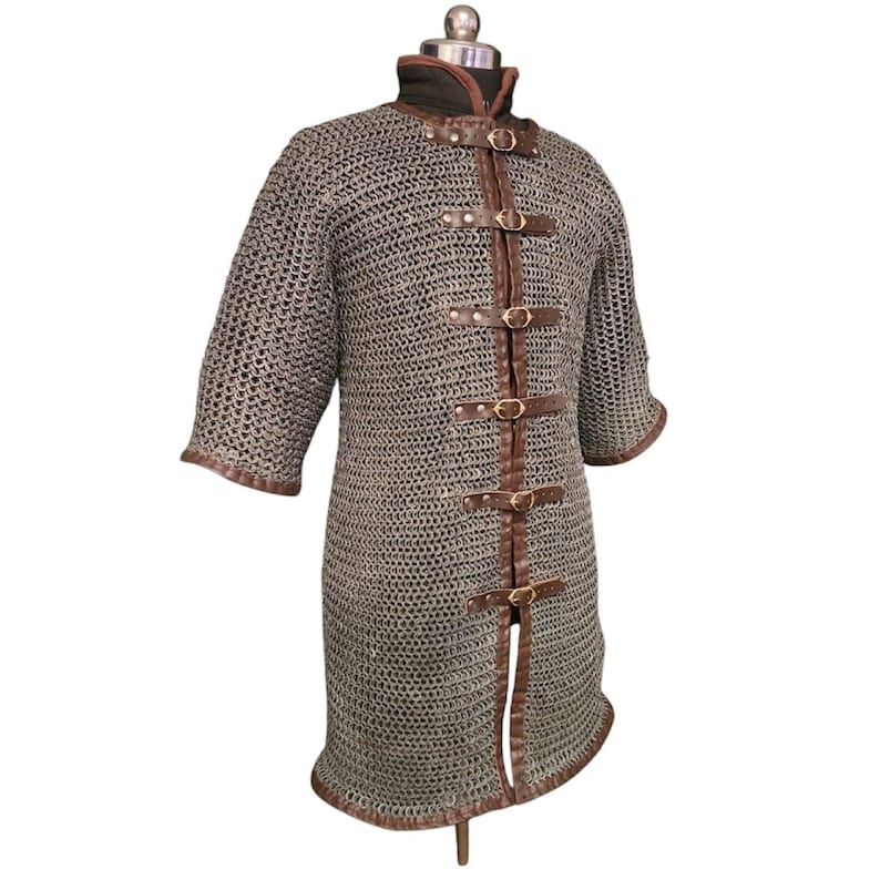 May include: A long, grey chainmail shirt with brown leather straps and buckles. The shirt has short sleeves and a pointed hem.