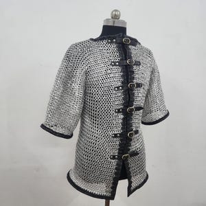 May include: A silver chainmail shirt with short sleeves and black leather trim. The shirt has a series of black leather straps with buckles down the front. The neckline and sleeve cuffs are also trimmed with black leather.
