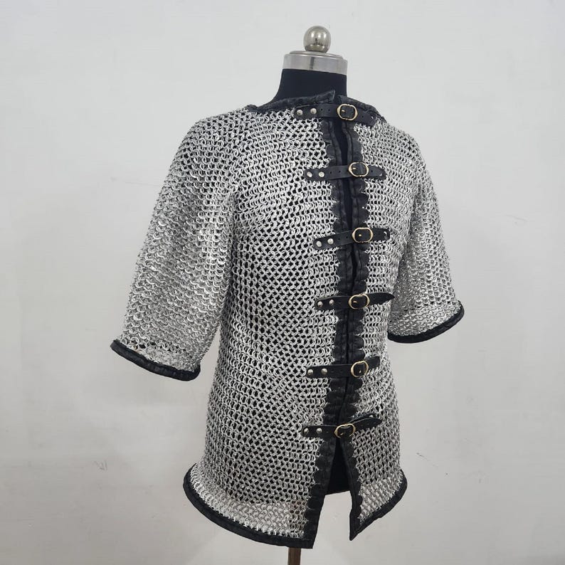 May include: A silver chainmail shirt with short sleeves and black leather trim. The shirt has a series of black leather straps with buckles down the front. The neckline and sleeve cuffs are also trimmed with black leather.