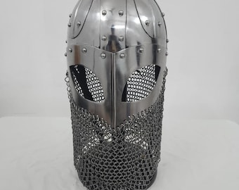 May include: A silver Viking helmet with a chainmail face mask. The helmet has a rounded top with rivets and a pointed nose guard.