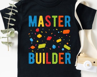 May include: Black t-shirt with the text "MASTER BUILDER" in colorful letters and a pattern of colorful toy building blocks.