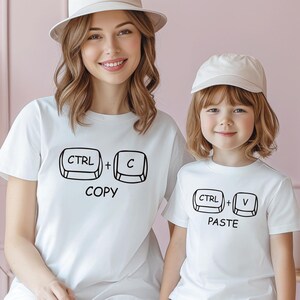 May include: A white t-shirt with the text "CTRL + C COPY" and a white t-shirt with the text "CTRL + V PASTE". The shirts are worn by a woman and a child.
