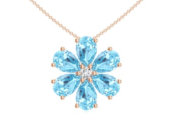 Puede incluir: Un collar de oro rosa con un colgante de flores. El colgante está compuesto por seis piedras preciosas de color azul claro en forma de lágrima que rodean una piedra central, redonda y transparente. La cadena del collar es delicada.