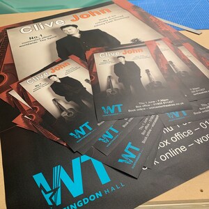 May include: A black poster with a blue and white logo for Huntingdon Hall. The poster advertises a concert by Clive John, a singer known as the "Voice of the critically acclaimed Johnny Cash Roadshow". The poster includes the text "No. 1 nominated album worldwide 'The Spirit'".