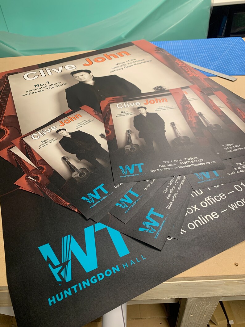 May include: A black poster with a blue and white logo for Huntingdon Hall. The poster advertises a concert by Clive John, a singer known as the "Voice of the critically acclaimed Johnny Cash Roadshow". The poster includes the text "No. 1 nominated album worldwide 'The Spirit'".