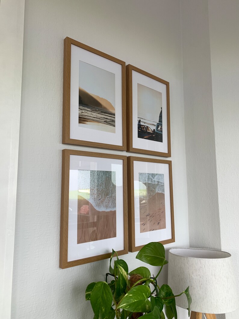 May include: Four framed photographs of beach scenes, arranged in a grid on a white wall. The photos feature a sandy beach, ocean waves, and a vintage car.