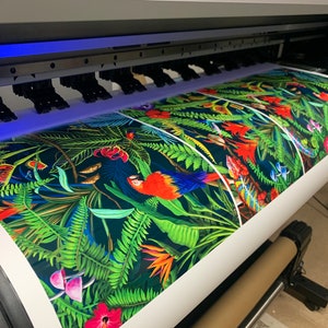 May include: A large format printer printing a colorful tropical pattern with parrots, flowers, and ferns on a white roll of paper.