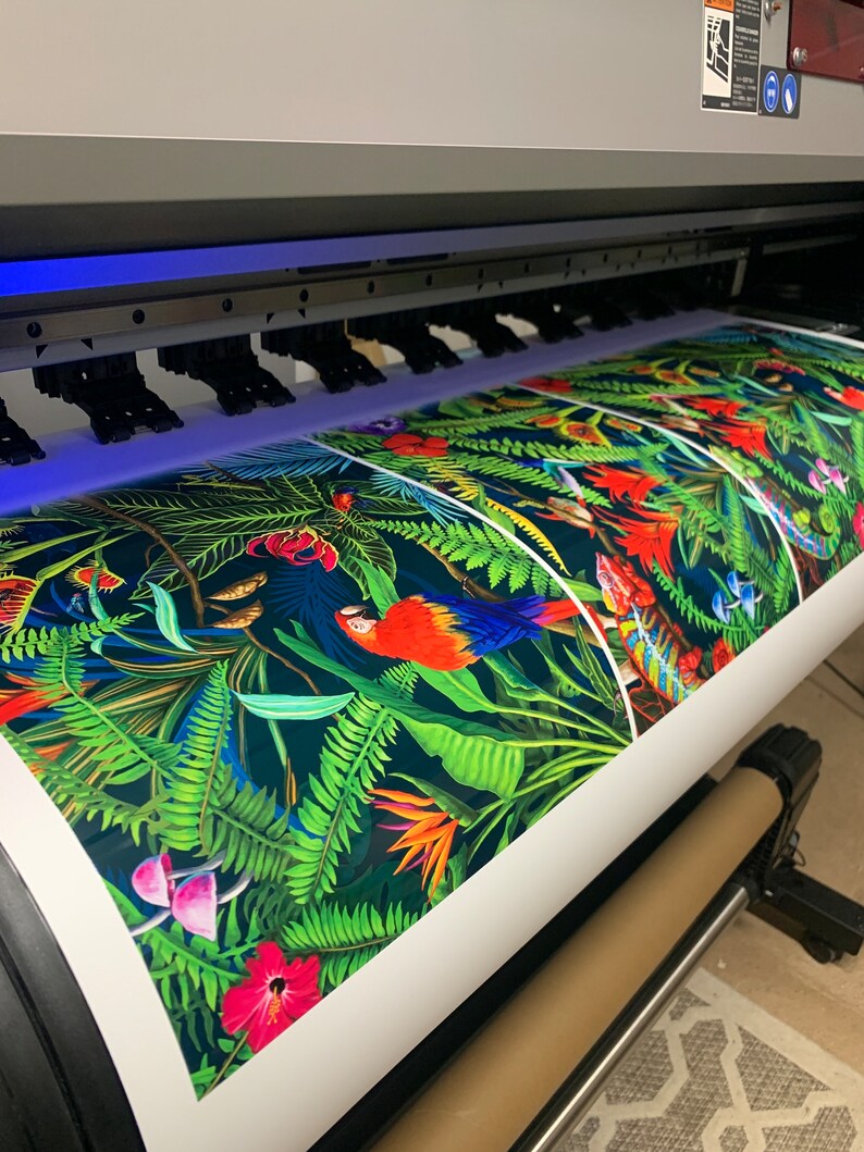 May include: A large format printer printing a colorful tropical pattern with parrots, flowers, and ferns on a white roll of paper.