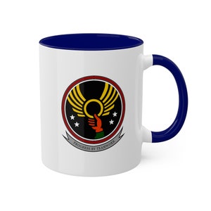May include: White ceramic coffee mug with a blue rim and handle. The mug features a black, yellow, red, and green logo with the text "Progress by Teamwork".