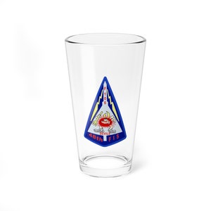 Puede incluir: Un vaso de pinta de vidrio transparente con un logotipo azul y rojo que presenta un personaje de dibujos animados y el texto "F-106 Devils 48th FIS".