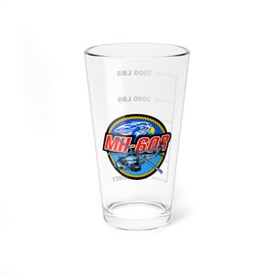 May include: A clear glass measuring cup with a blue, yellow, and red graphic of a helicopter and an eagle with the text "MH-60R" on it. The cup has markings for 2000 lbs and 3000 lbs.