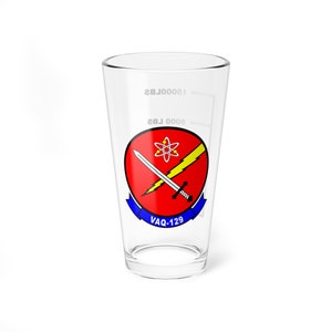 May include: A clear glass pint glass with a red, yellow, and blue squadron emblem. The emblem features a crossed sword and lightning bolt with an atom symbol in the center. The text "VAQ-129" is printed below the emblem.