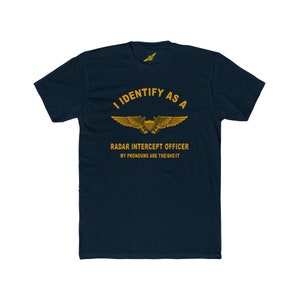 Peut inclure: Un t-shirt bleu marine avec un graphique doré d'une insigne ailée et le texte "Je m'identifie comme un officier d'interception radar. Mes pronoms sont le/elle/il."
