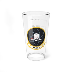 Peut inclure: Un verre à bière en verre transparent avec un motif de crâne et d'os croisés noir et blanc. Le motif est entouré d'un cercle jaune avec le texte "VF-151" en dessous. Le verre est marqué pour 16oz et 20oz.