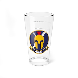 May include: A clear glass pint glass with a blue and yellow graphic of a Spartan helmet with crossed spears and lightning bolts. The text "VAQ-131" is printed below the graphic.