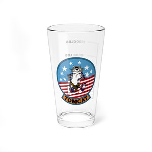 May include: A clear glass pint glass with a graphic of a cartoon cat wearing a camouflage uniform and a red, white, and blue American flag. The text "TOMCAT" is printed below the cat.
