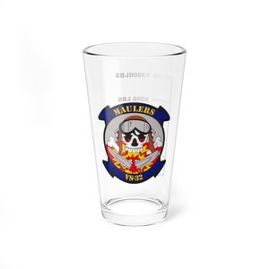 May include: A clear glass pint glass with a blue and yellow logo featuring a skull wearing a pilot's helmet and goggles. The logo says "Maulers VS-32".