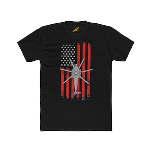 May include: Black t-shirt featuring a red, white and blue American flag design. A grey helicopter silhouette is centred on the flag.