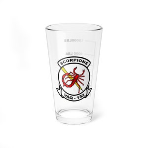 May include: A clear glass pint glass with a white graphic of a red scorpion with a yellow lightning bolt. The text "SCORPIONS" and "VAQ-132" are printed on the glass.