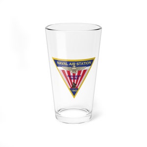 May include: A clear glass pint glass with a gold, red, white, and blue logo that reads "NAVAL AIR STATION PATUXENT RIVER 1943".