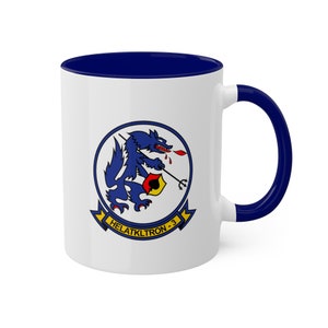 May include: White ceramic mug with a navy blue interior and handle. The mug features a circular emblem with a blue wolf holding a trident and a banner that reads "HELATKLTRON-3".