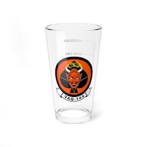 May include: A clear glass pint glass with a red, black, and yellow graphic of a devil's head with horns and a halo. The graphic is surrounded by a black circle with the text "VAQ-144" in white letters.