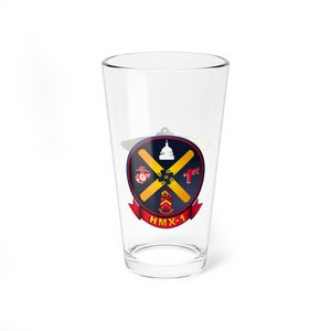 May include: A clear glass pint glass with a printed design of the HMX-1 squadron insignia. The insignia features a red, white, and blue shield with a crossed propeller, a capitol building, and the text "1st" and "HMX-1".