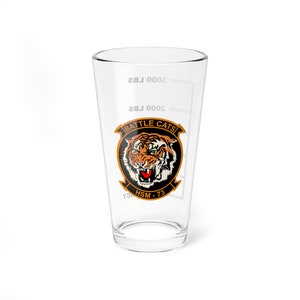 May include: A clear glass pint glass with a black and orange tiger head graphic. The graphic includes the text "BATTLE CATS" and "HSM - 73".