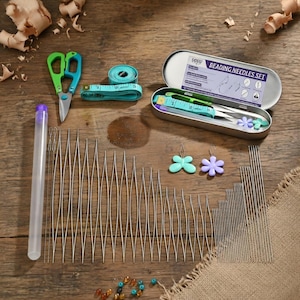 May include: A beading kit with various tools on a wooden surface. The kit includes a metal case labelled "Beading Needles Set", scissors, a measuring tape, and a collection of needles. Also included are two flower-shaped charms.