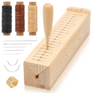 Puede incluir: Una herramienta de ranurado de costura de cuero de madera con un mango de madera, una cuchilla de metal y una serie de agujeros numerados. La imagen también muestra carretes de hilo negro, marrón y beige, agujas y un dedal.