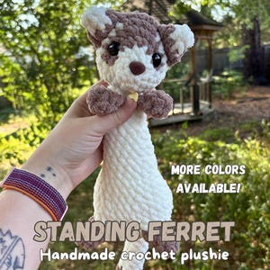 May include: A handmade crochet plushie of a standing ferret with white and brown yarn. The ferret has black eyes, a brown nose, and a small yellow collar. Text on the image reads: MORE COLORS AVAILABLE! STANDING FERRET Handmade crochet plushie.
