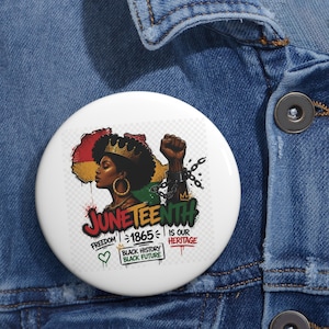 May include: A round pinback button featuring a graphic of a person with an afro wearing a crown, a raised fist with broken chains, and the text JUNETEENTH FREEDOM 1865 IS OUR HERITAGE BLACK HISTORY BLACK FUTURE with a heart and crown icon.
