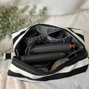 May include: Black and white striped cosmetic bag with a black and white gingham interior. The bag is open, revealing a hair styling tool and accessories. The bag has a zipper closure and a small handle.