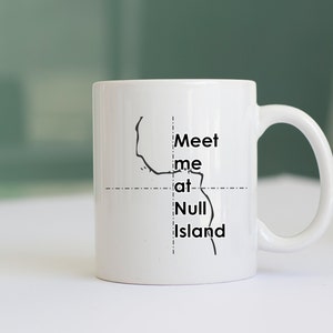 May include: White ceramic mug with a black outline of an island and the text "Meet me at Null Island". The mug has a curved handle and is set against a soft green background. A simple, yet unique design.