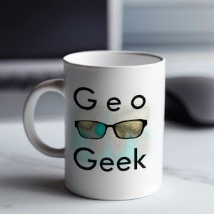 Puede incluir: Taza de cerámica blanca con las palabras "Geo Geek" en texto negro. La palabra "Geo" está sobre un par de gafas de sol con un patrón de mapa del mundo. Las gafas de sol son de color azul turquesa.
