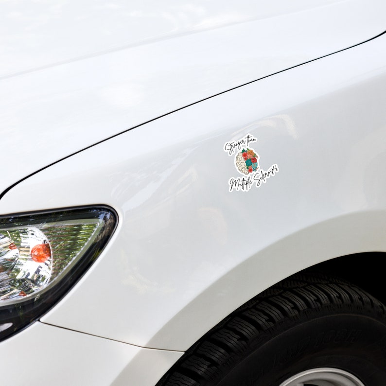 Op de afbeelding: Witte auto met een sticker aan de zijkant met de tekst "Sterker dan Multiple Sclerose" met een hersengrafiek met bloemen.