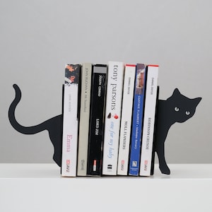 May include: Black metal bookends shaped like a cat holding up a stack of books. The books include titles like "Robinson Crusoe", "Moll Flanders", "Lord Jim", "Emma", and "Mr. Standfast".
