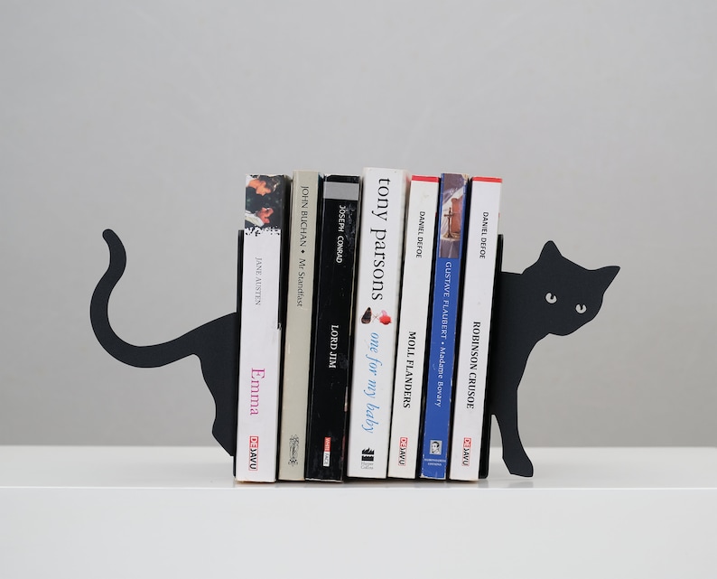 May include: Black metal bookends shaped like a cat holding up a stack of books. The books include titles like "Robinson Crusoe", "Moll Flanders", "Lord Jim", "Emma", and "Mr. Standfast".