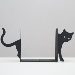 May include: Black metal bookends shaped like cats peeking around a corner. The bookends are a modern and stylish way to organize books on a shelf.
