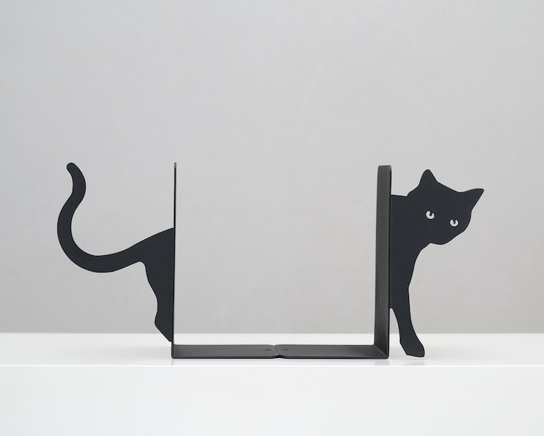May include: Black metal bookends shaped like cats peeking around a corner. The bookends are a modern and stylish way to organize books on a shelf.