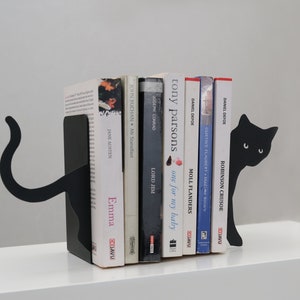 May include: Black metal cat bookends holding a row of books with titles like "Emma", "Lord Jim", "Moll Flanders", and "Robinson Crusoe".