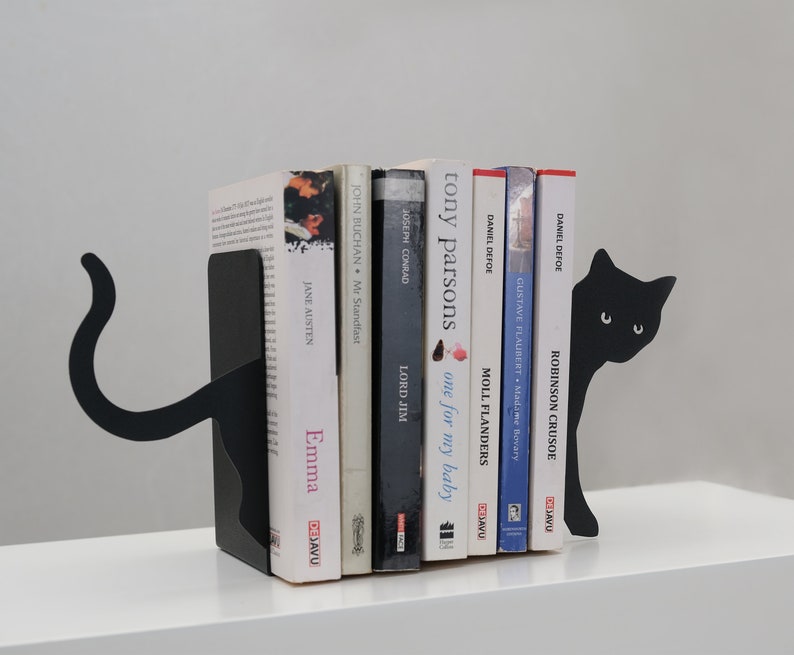 May include: Black metal cat bookends holding a row of books with titles like "Emma", "Lord Jim", "Moll Flanders", and "Robinson Crusoe".